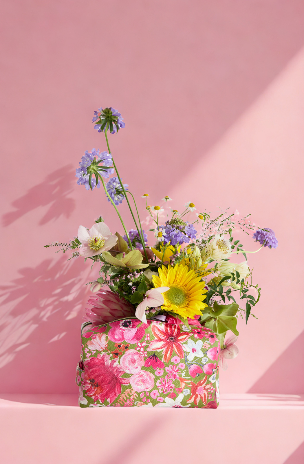 Floral arrangement in a patterned handbag against a pink background