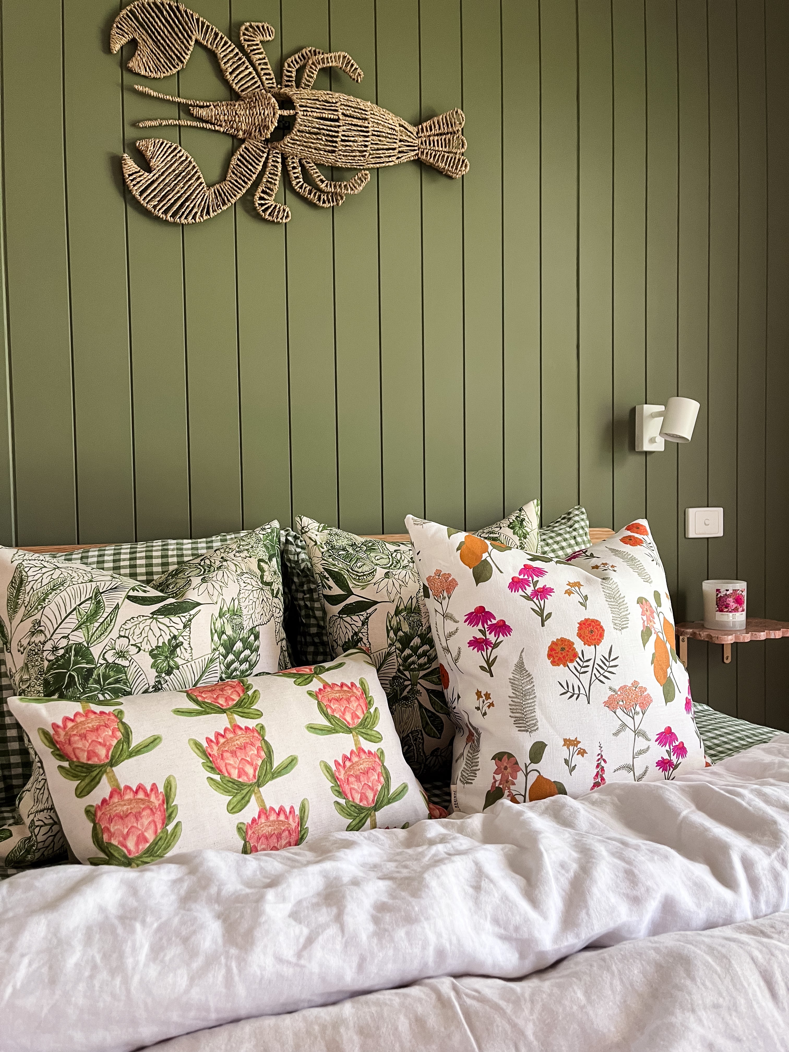 Dancing With Juniper summer collection cushions sitting on a bed in front of a green panelled wall